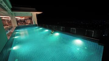 Una piscina con pavimento piastrellato, circondata da un balcone che offre vista sulla città di notte.