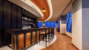 Zona de bar con mostrador curvo, taburetes y una estantería con botellas.