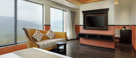 A hotel room with a large bed, a sofa, a TV mounted on the wall, and a fireplace.