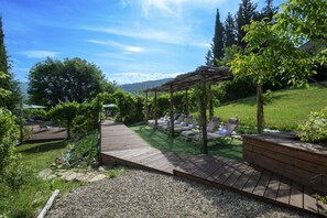 A wooden deck with lounge chairs and a pergola, surrounded by greenery and a clear sky. - Villa Chianti | Luxury Pool, Jacuzzi Tub, Sauna and Chromoterapy (Greve in Chianti)