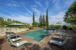 A swimming pool with lounge chairs and umbrellas, surrounded by greenery and a stone wall. - Villa Chianti | Luxury Pool, Jacuzzi Tub, Sauna and Chromoterapy (Greve in Chianti)
