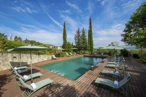 A swimming pool with lounge chairs and umbrellas, surrounded by greenery and a stone wall.