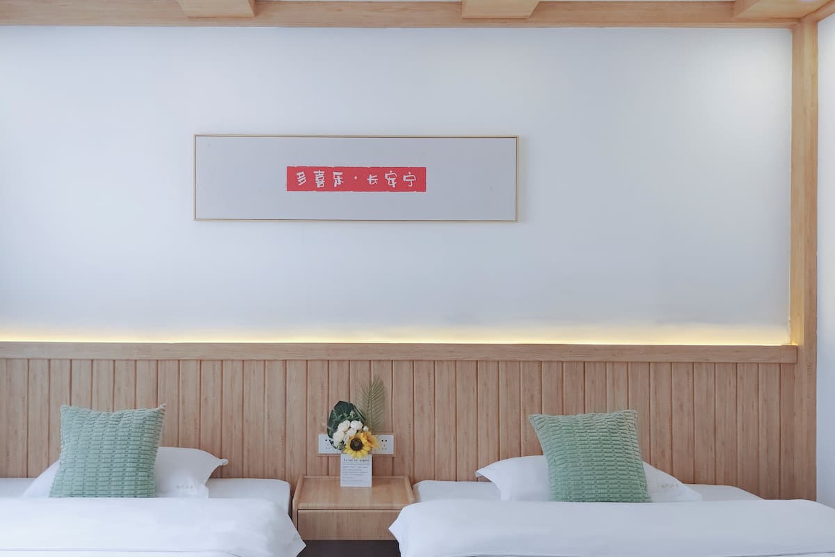 A hotel room with two beds, a wooden headboard, a framed sign on the wall, and a small table with a vase of flowers.