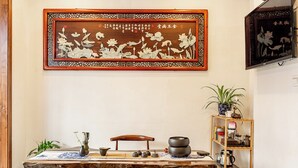 Een kamer in traditionele Chinese stijl met een houten tafel, een kunstwerk met kalligrafie en een plank met diverse objecten.