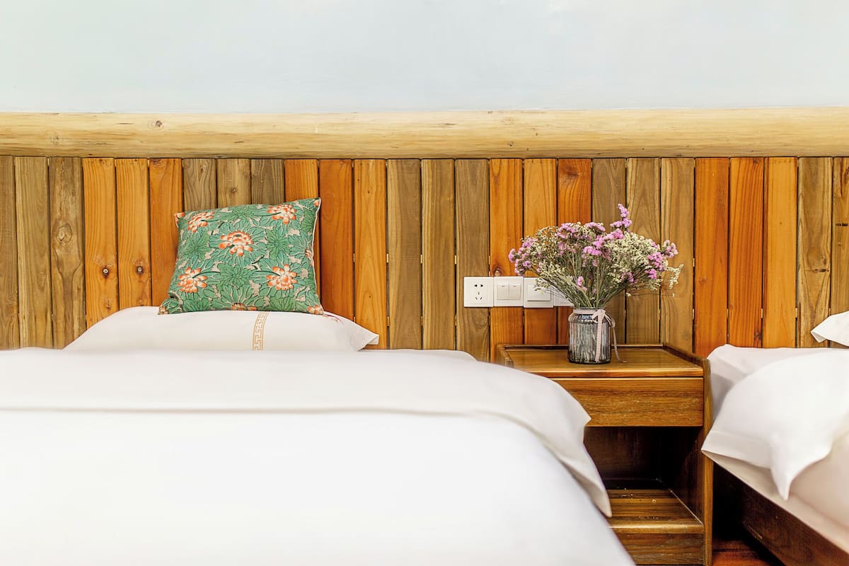 A bedroom with two beds, a wooden headboard, a nightstand with a vase of flowers, and a power outlet.