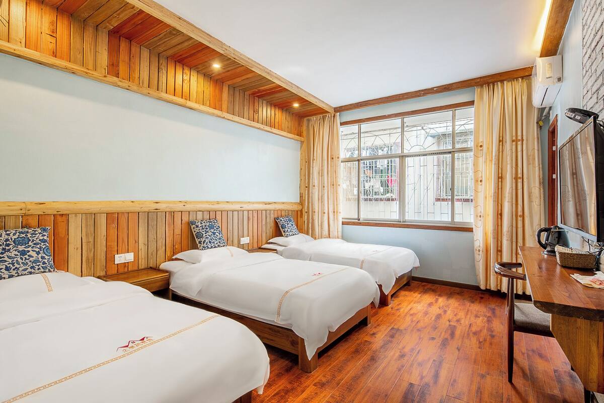 A hotel room with wooden paneling, two beds, a wooden desk, and a large window with curtains.