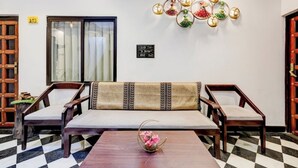 A room with a checkered floor, a sofa with patterned cushions, a small table with a vase of flowers, and wall decorations. - Lake N Hill View (Udaipur)