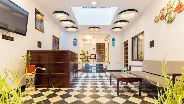 A hotel lobby with a checkered floor, a reception desk, a sofa, a TV, and a ceiling with recessed lighting. - Lake N Hill View (Udaipur)