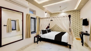 A bedroom with a bed, a ceiling fan, a TV, and a large mirror. - Lake N Hill View (Udaipur)