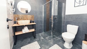A modern bathroom with a glass shower enclosure, a white toilet, a round mirror, and a wooden shelf with towels. - Ataraxya Premium Residence (Brasov)