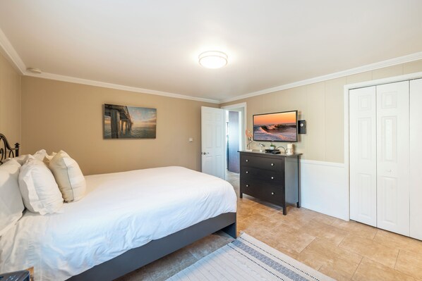 Un dormitorio con una cama, un tocador, un televisor y una puerta.
