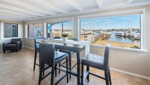 Ein geräumiges Zimmer mit großem Fenster und Blick auf eine Marina, einem Essbereich mit Tisch und Stühlen sowie einer gemütlichen Sitzecke mit Sessel.