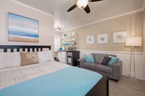 A bedroom with a bed, a gray sofa, a desk, and a ceiling fan.