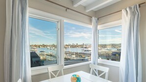 A dining area with a table and chairs, large windows with curtains, and a view of a marina with boats. - Stylish Newport Condos w/ Dock Access, Walk to Balboa Fun Zone & Beach (Newport Beach)