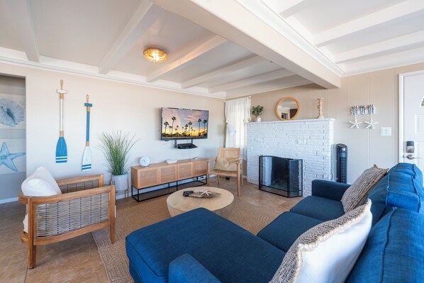 A modern living room with a sofa, a coffee table, a TV, a fireplace, and a decorative wall with a painting and wall-mounted items.