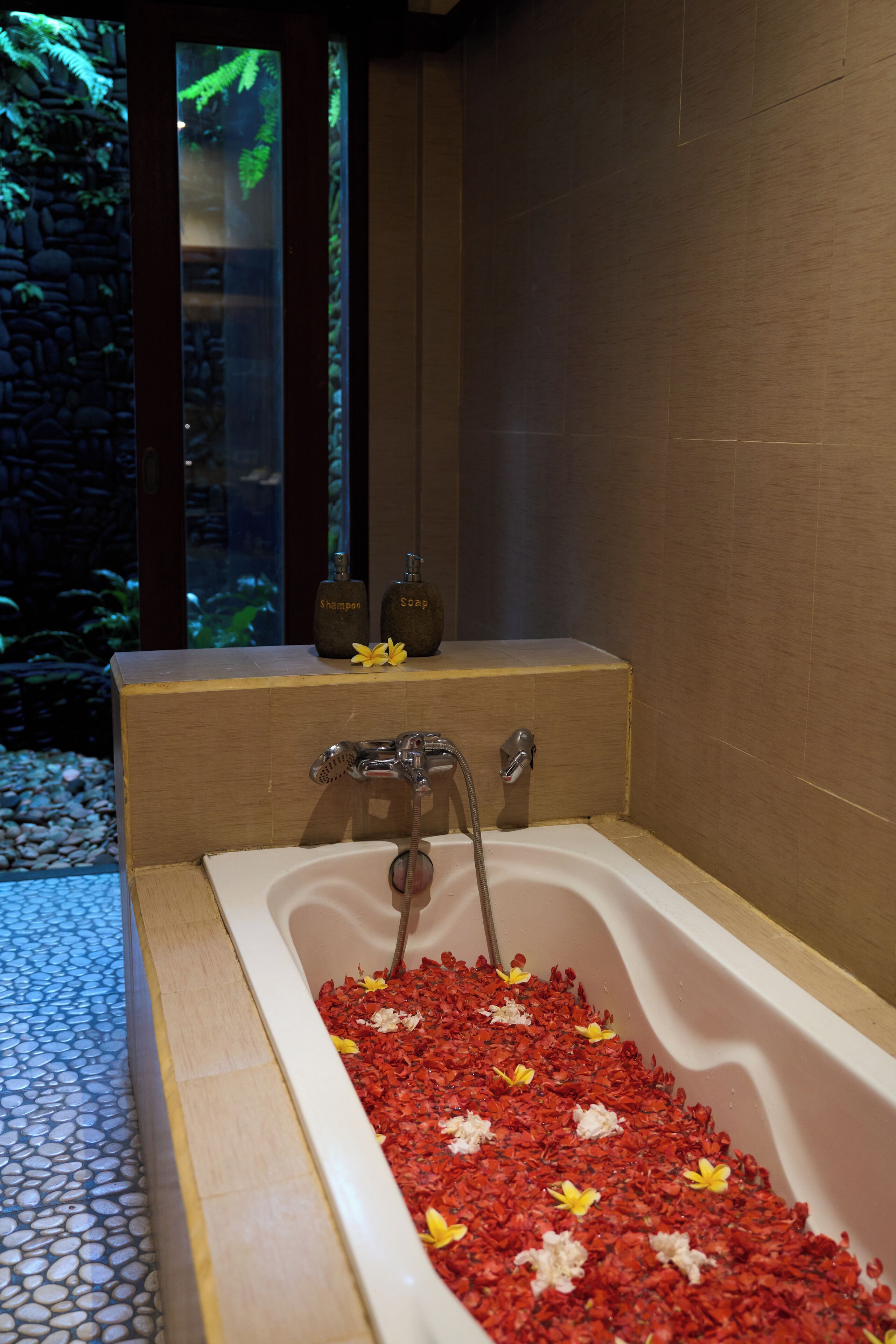 A bathtub filled with red flower petals and two bottles of shampoo and soap on the side.