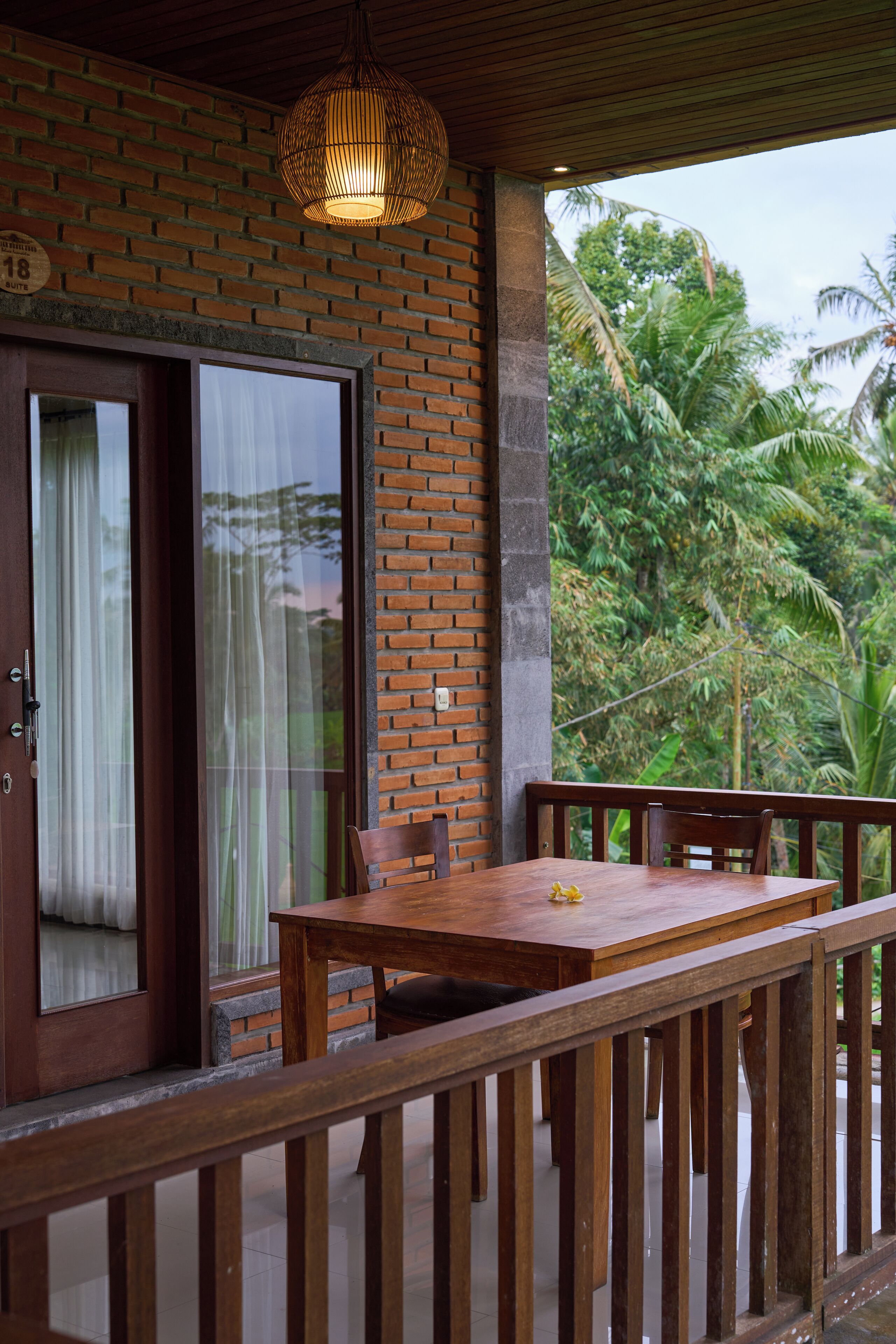 A wooden table and chairs on a balcony with a brick wall and a hanging light fixture.