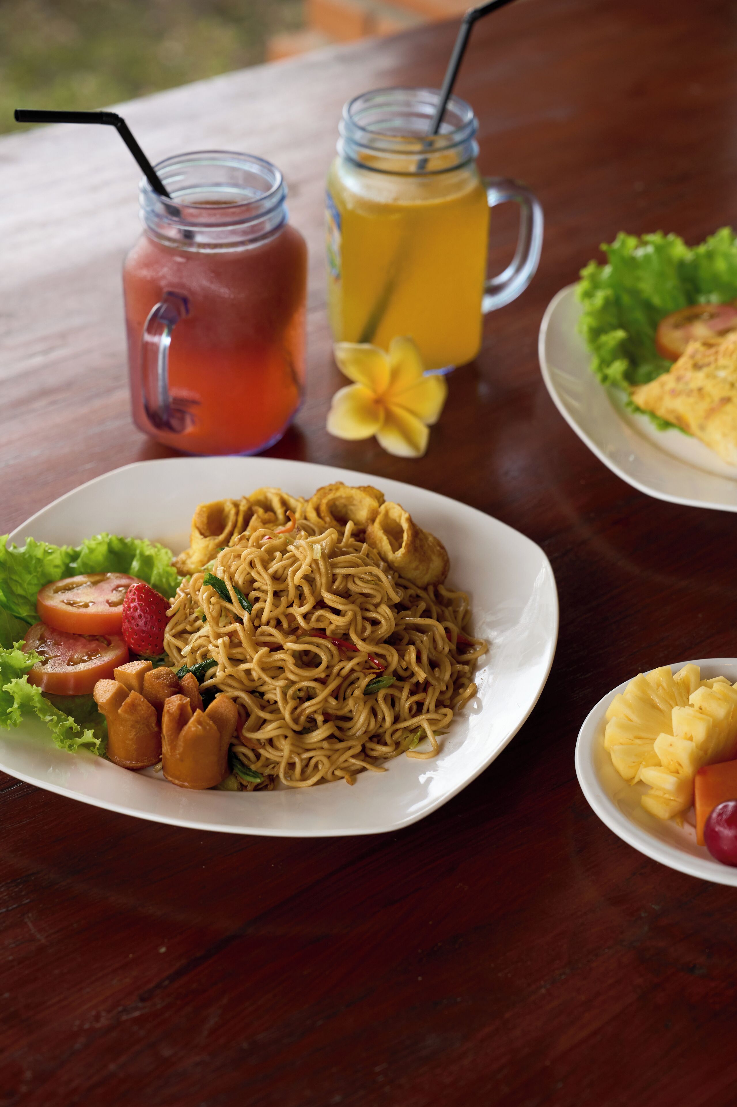 A table with a plate of noodles, a glass of iced tea, and a glass of orange juice.