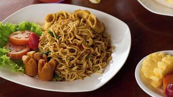 A table with a plate of noodles, a glass of iced tea, and a glass of orange juice.