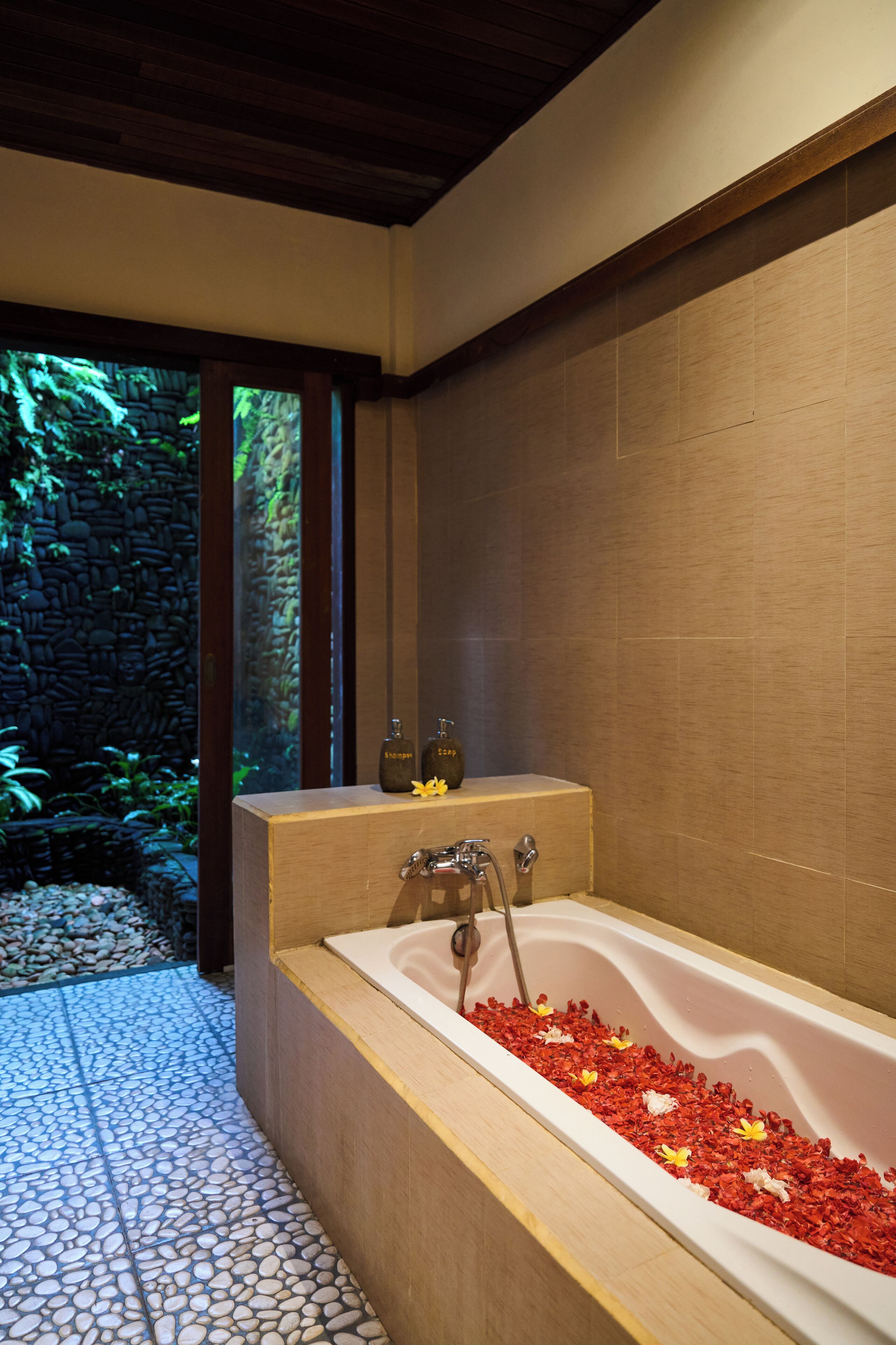 A modern bathroom with a freestanding bathtub, a stone wall, and a tiled floor.