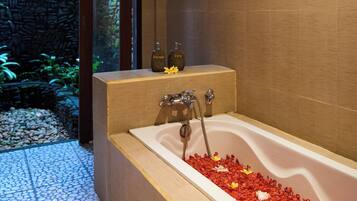 A modern bathroom with a freestanding bathtub, a stone wall, and a tiled floor.