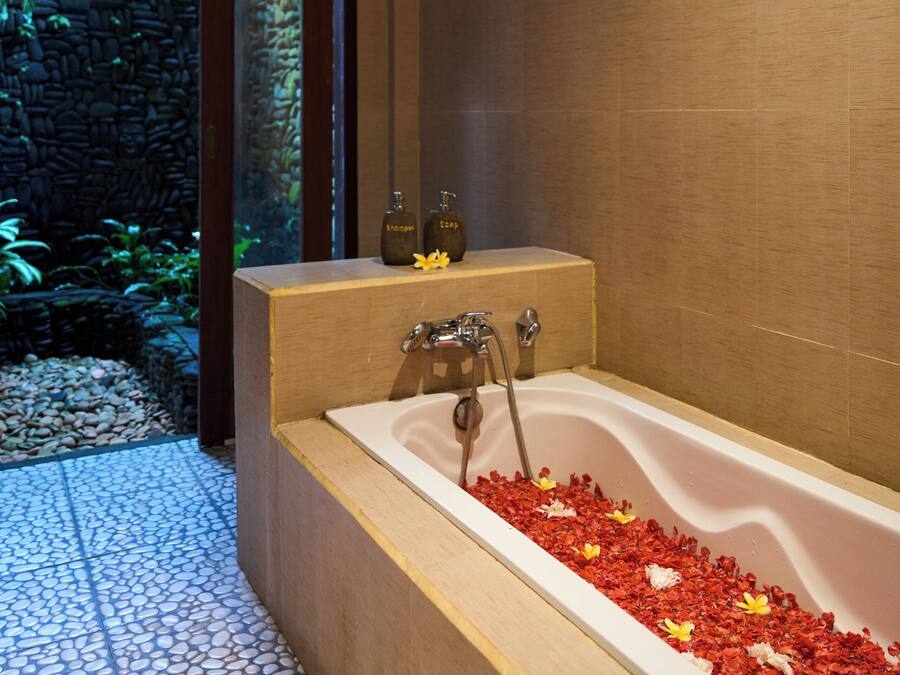 A modern bathroom with a freestanding bathtub, a stone wall, and a tiled floor.