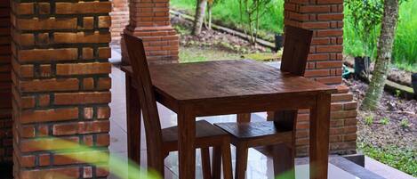Un área de comedor al aire libre techada, con pilares de ladrillo y una mesa de madera.