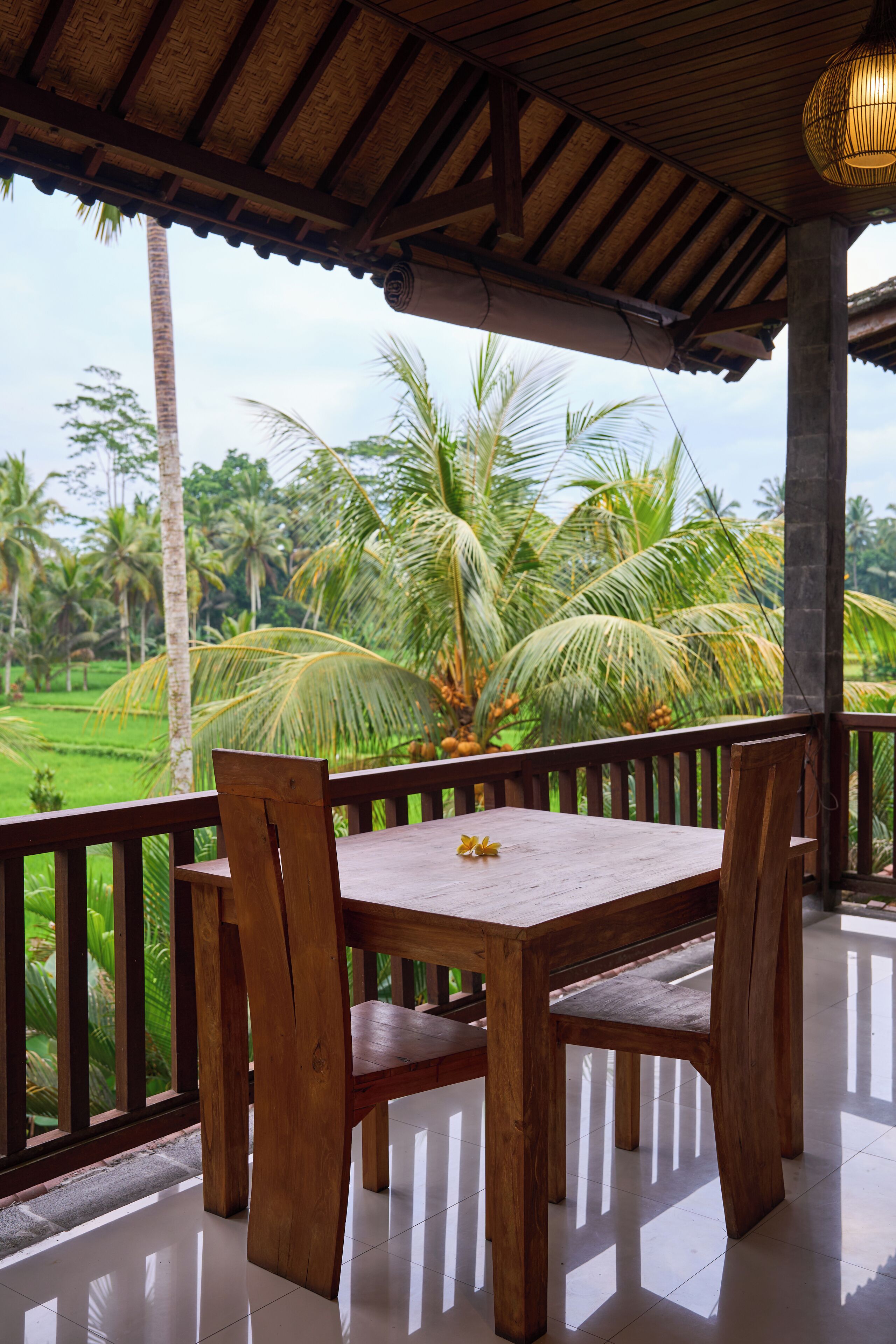A wooden table and chairs on a balcony with a view of palm trees and a garden.