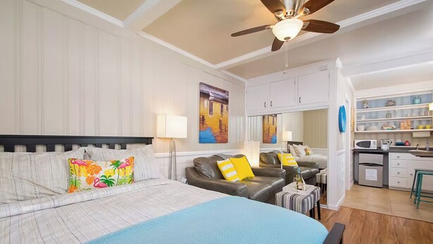 A modern hotel room with a large bed, a sofa, a dining area, and a kitchen.
