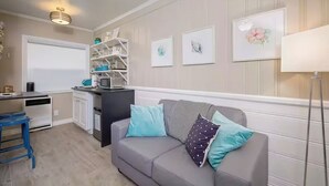 A living room with a grey sofa, a kitchen area with white cabinets, and a dining table.