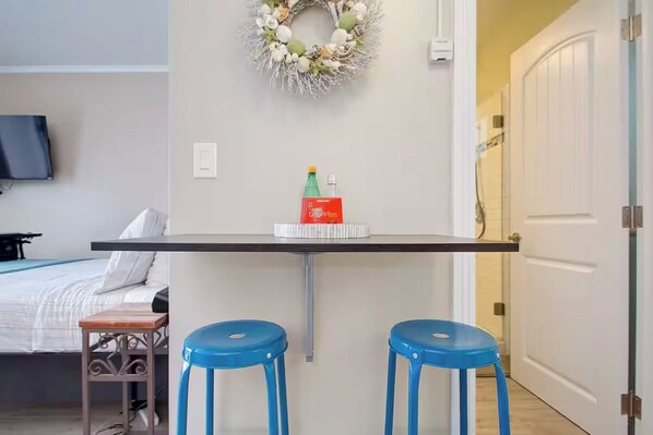 A small kitchenette with a bar stool, a bottle of soda, and a box of tissues on the counter.