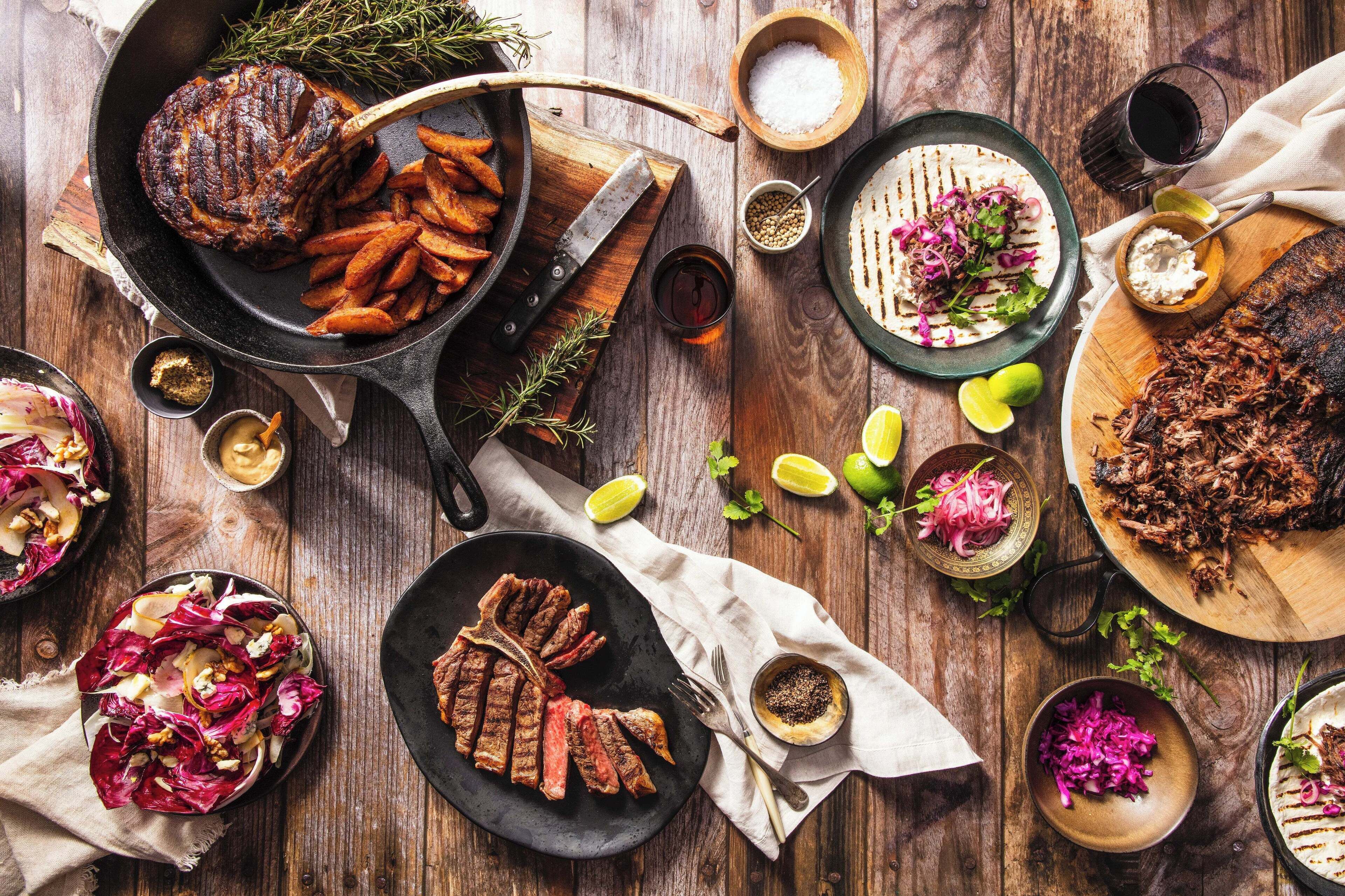A variety of grilled meats and vegetables on a wooden table.