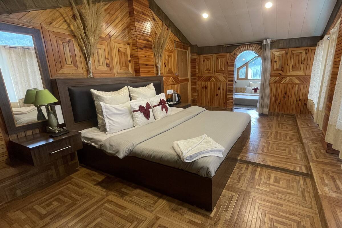 Un dormitorio con una cama grande, paneles de madera, una mesita de noche, una lámpara y vistas a través de un arco.