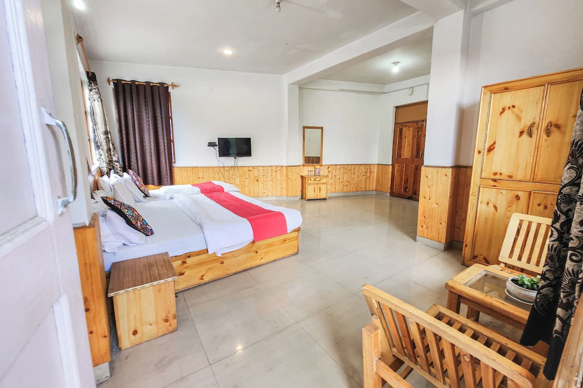 Habitación de hotel con cama de madera, una mesita pequeña, una silla, televisor y armario.
