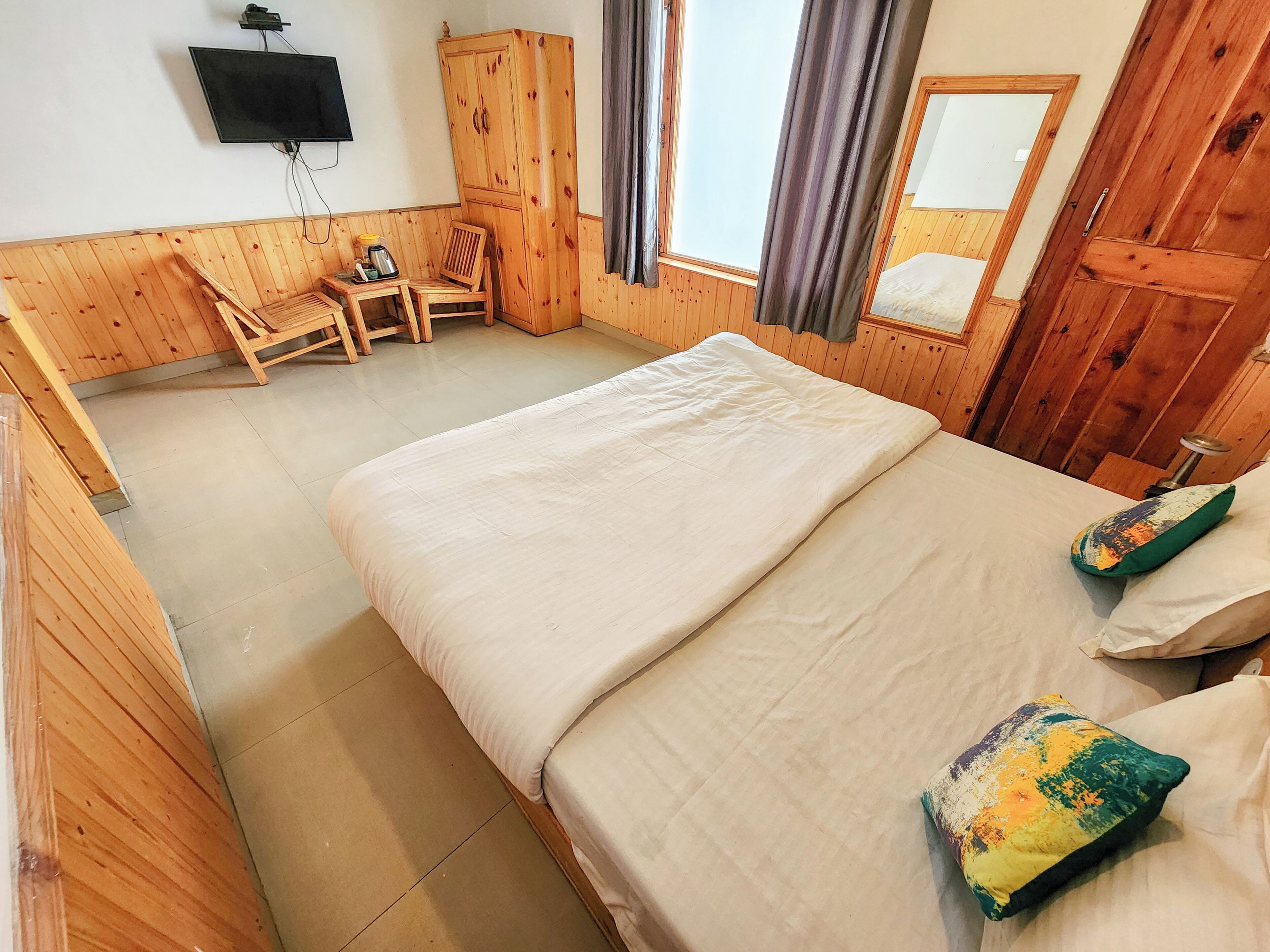 A wooden-paneled room with a bed, a chair, a small table, and a television mounted on the wall.