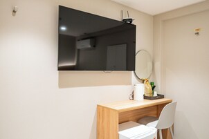 Una habitación pequeña y moderna con un escritorio de madera, una silla blanca, un espejo y un televisor de pantalla plana montado en la pared.
