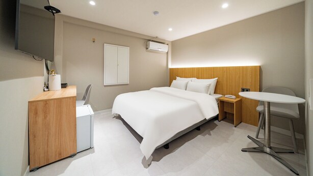 A modern hotel room with a bed, bedside table, a small desk, a chair, a round table, and a flat-screen TV mounted on the wall. - Cream Hotel (Guri)