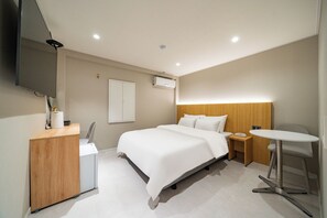 Ett modernt hotellrum med en säng, ett nattduksbord, ett litet skrivbord, en stol, ett runt bord och en platt-TV som är monterad på väggen.