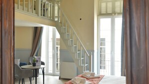A bedroom with a bed, a desk, and a chair. There is a staircase leading to an upper level.