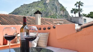 A table with two wine glasses and a bottle, a cushion, and a view of a hill with a building on top.