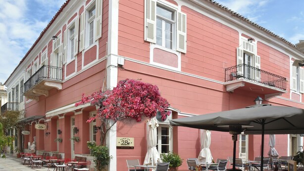A pink building with white trim, a balcony, and outdoor seating with umbrellas.