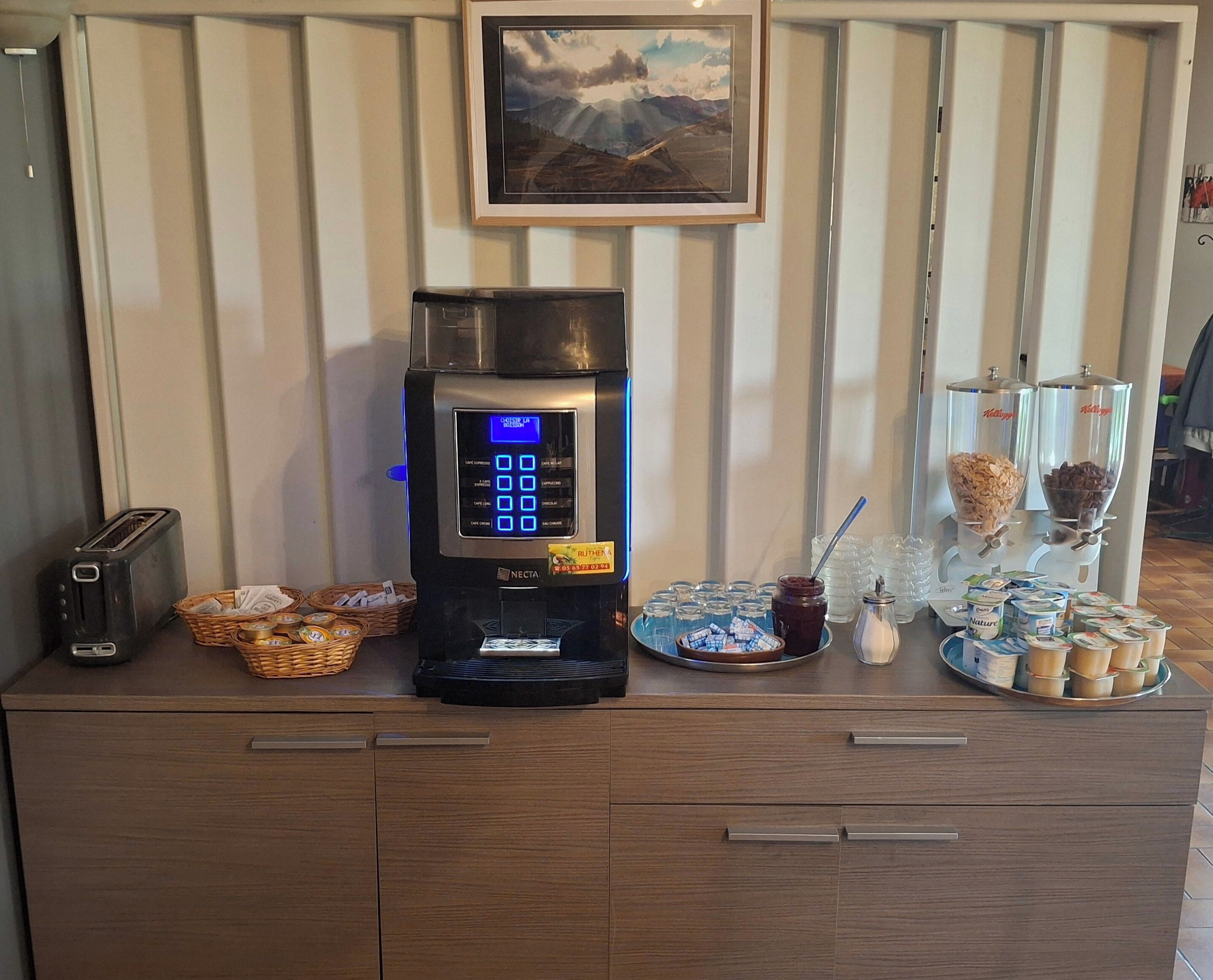 A self-service coffee station with a digital coffee maker, a toaster, and various food items like yogurt and granola.