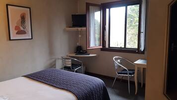 Un dormitorio con cama, escritorio, silla, televisor y ventana.