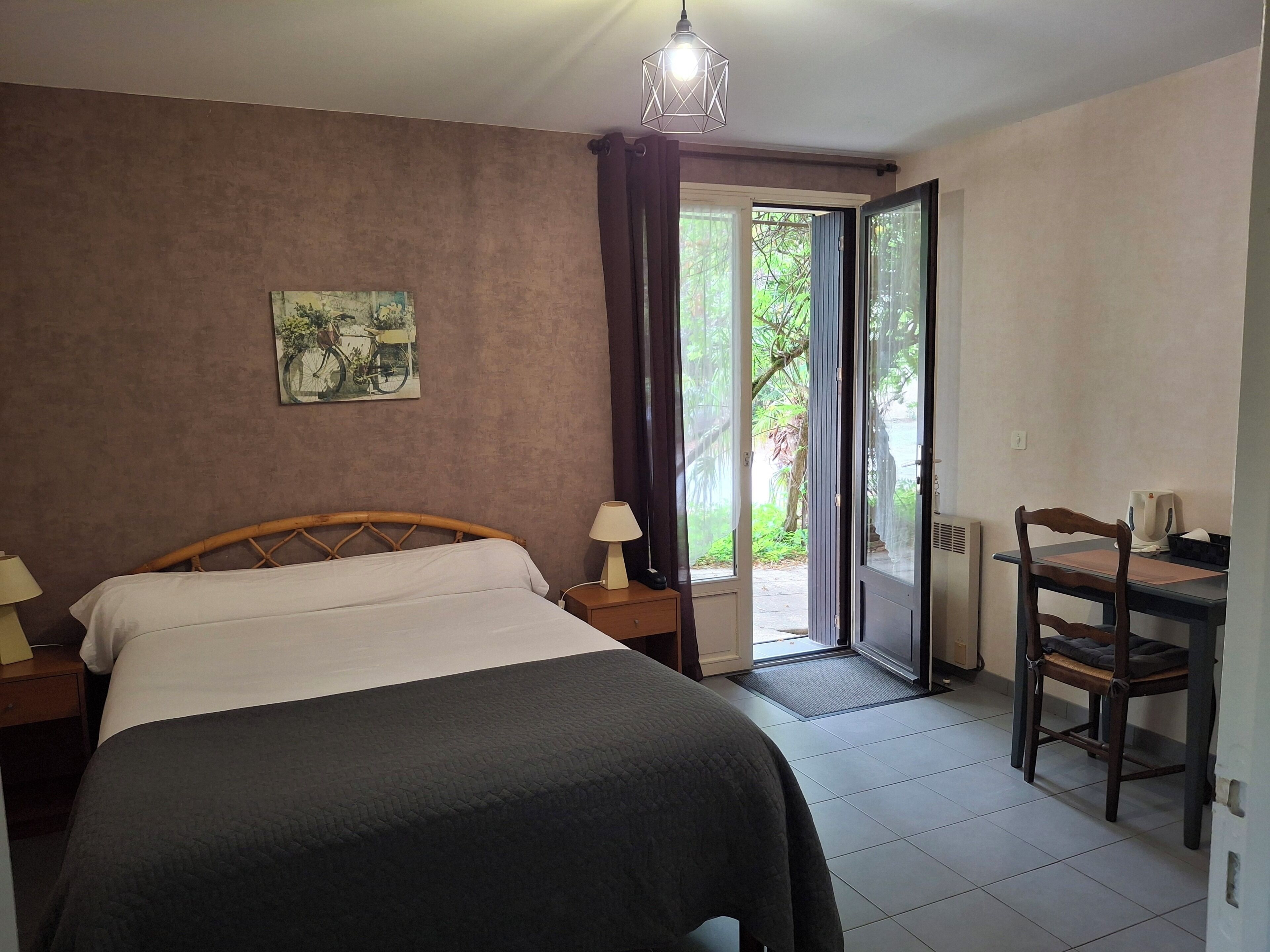 Ein Schlafzimmer mit einem Bett, einem Schreibtisch und einem Stuhl. Es gibt ein Fenster mit Vorhängen, eine Tür und eine Wandleuchte.