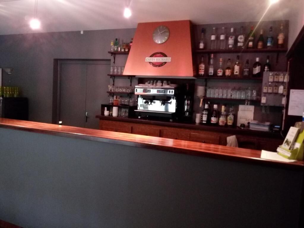 A bar area with a coffee machine, shelves with bottles, and a clock on the wall.