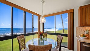 Ein Essbereich mit einem Glastisch und Korbstühlen, mit Blick auf einen Strand und den Ozean.