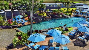 A pool area with lounge chairs and umbrellas, surrounded by tropical plants and a view of the landscape.