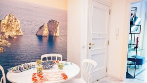 A dining area with a round table, white chairs, and a view of rocky cliffs and water. - CapriGetaway - Domus Le Botteghe (Capri)