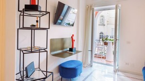 A modern living room with a glass coffee table, a blue ottoman, and a mounted TV. - CapriGetaway - Domus Le Botteghe (Capri)