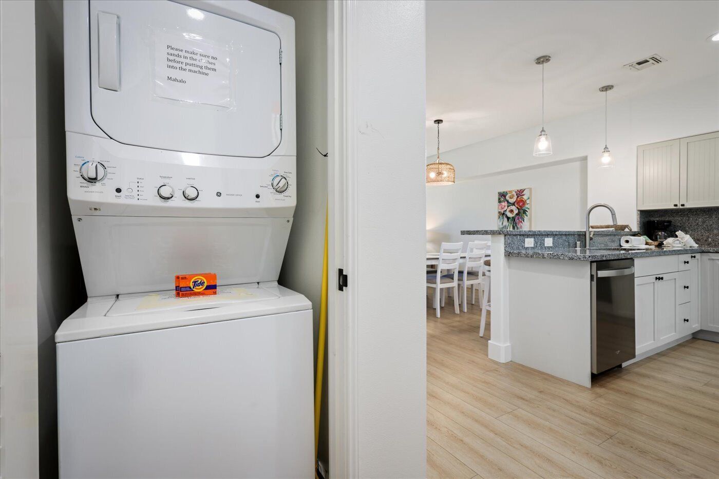 A modern kitchen with a built-in washer and dryer, a dining area with a table and chairs, and pendant lighting.